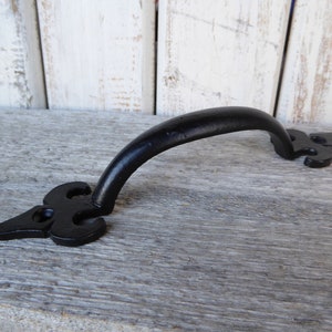 May include: Black metal door handle with a decorative, ornate design. The handle is curved and has a smooth finish.