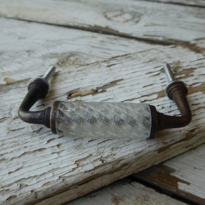 May include: A clear glass cabinet knob with a twisted design and a bronze finish. The knob has a metal screw on each end.