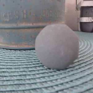 May include: A gray, round, smooth stone on a blue and white patterned surface.