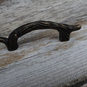 May include: Bronze-toned cabinet pull handle with a textured, branch-like design. The curved handle is approximately 5 inches long, with a detailed, organic appearance. Ideal for adding a rustic or natural touch to furniture or cabinetry.