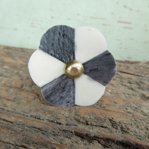 May include: A black and white flower-shaped cabinet knob with a gold center. The knob is made of bone or wood and has a geometric pattern.