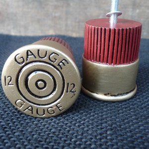 May include: Two gold and red shotgun shell drawer pulls with a black "12 Gauge" inscription.