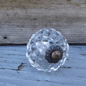May include: Two clear glass cabinet knobs with a textured, diamond-like pattern. The knobs have a brass-colored metal base.