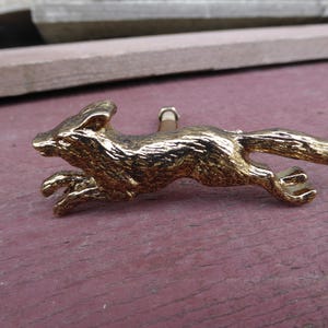 May include: A gold-colored metal fox figurine in a running pose. The fox has a detailed design and is a decorative piece.