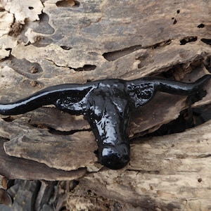 May include: A black ceramic bull's head with horns, painted in a glossy finish. The bull's head is sitting on a piece of weathered wood.
