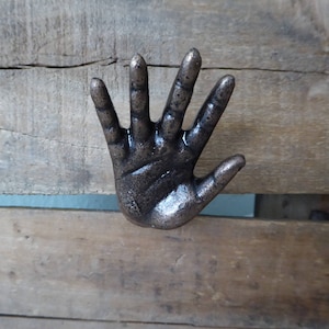 May include: A cast iron hand-shaped door knocker with a dark bronze finish.