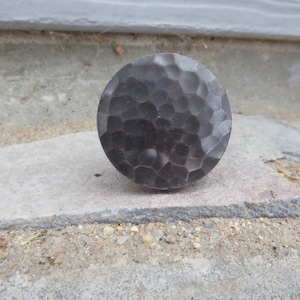 May include: A round, hammered metal knob with a dark gray finish. The knob has a textured surface and is made of metal.
