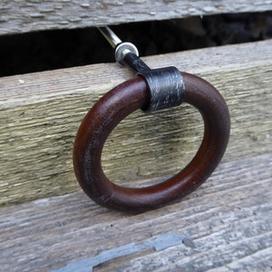 May include: A dark brown wooden ring pull handle with a black metal band and a silver screw. The handle is attached to a wooden surface.