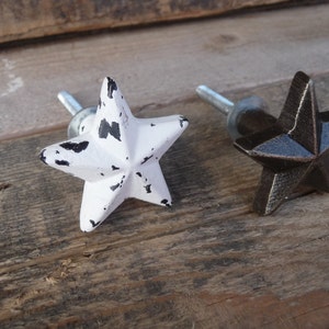 May include: Two star-shaped cabinet knobs, one white with black distressing and one dark brown, both with silver screws.