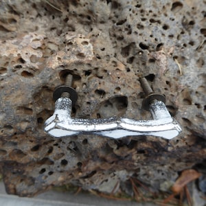 Peut inclure: Une paire de poignées de tiroir argentées avec un design texturé. Les poignées sont montées sur une surface rocheuse brune et rugueuse.