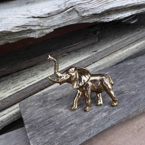 May include: A gold-colored elephant figurine with its trunk raised in the air. The figurine is sitting on a wooden surface.