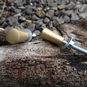 May include: Two gold-toned cabinet knobs with silver screws and washers. The knobs are on a piece of weathered wood.
