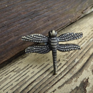 May include: A bronze dragonfly-shaped cabinet knob with detailed wings and a textured body.