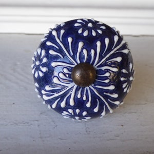 May include: A blue ceramic knob with a white floral design. The knob has a brass screw in the center.