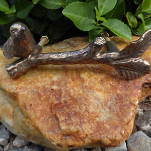 May include: A rustic bronze cabinet pull featuring a stylized tree branch with two birds perched on it. The branch has a leaf design at the end.