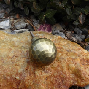 May include: A hammered brass knob with a round, textured surface. The knob is a dark gold color and has a short stem.