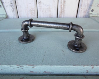 May include: A silver metal pipe-style drawer pull with a rounded rectangular shape. The pull has a rustic, industrial look.