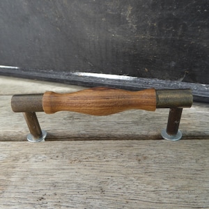May include: A wooden drawer pull with brass accents. The pull has a rounded, slightly curved wooden handle and two brass end caps.