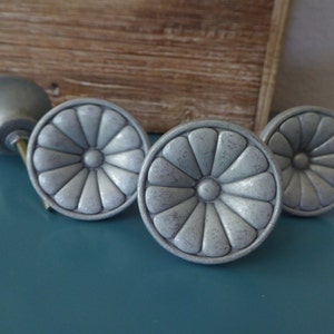 May include: Four silver-toned cabinet knobs with a decorative flower design. The knobs have a slightly distressed finish.
