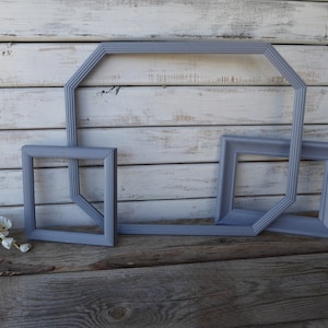 May include: Three gray picture frames of different sizes and shapes. The largest frame is octagonal, the middle frame is square, and the smallest frame is rectangular. The frames are all made of wood and have a distressed finish.