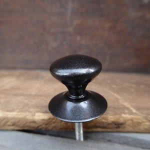 May include: A black cabinet knob with a round top and a flat base. The knob has a shiny, metallic finish.