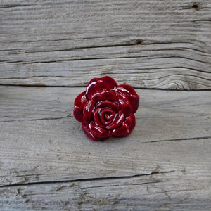 May include: A deep red ceramic rose flower with a glossy finish. The rose is a decorative accent for a home or garden.