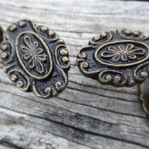 Peut inclure: Deux boutons de cabinet ovales de style antique avec un motif floral décoratif. Les boutons sont en métal et ont une finition bronze foncé.