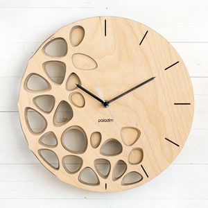May include: A wooden wall clock with a unique design featuring a circular cutout pattern. The clock has black hands and a simple black "paladin" logo.