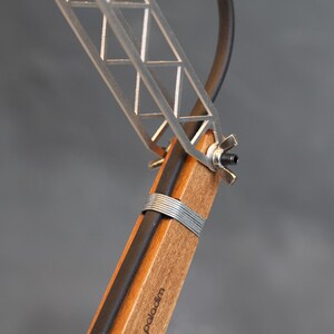 Peut inclure: Gros plan sur une lampe de bureau moderne. La lampe a une base en bois avec un cordon noir et un cadre en m&eacute;tal argent&eacute;. Le cadre a un design g&eacute;om&eacute;trique. Le mot "paladim" est imprim&eacute; sur la base en bois.