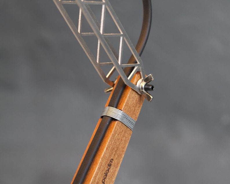 Peut inclure: Gros plan sur une lampe de bureau moderne. La lampe a une base en bois avec un cordon noir et un cadre en m&eacute;tal argent&eacute;. Le cadre a un design g&eacute;om&eacute;trique. Le mot "paladim" est imprim&eacute; sur la base en bois.