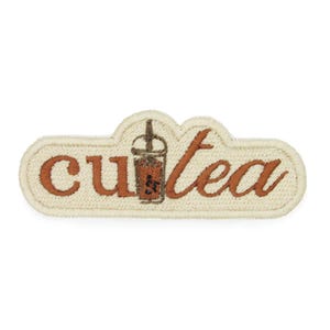 May include: A beige embroidered patch with the text "cutea" in brown cursive lettering. A brown cartoon illustration of a boba tea cup with a straw is centered between the words.