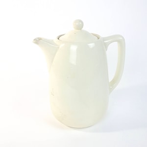 May include: A white ceramic coffee pot with a lid and a handle. The pot is smooth and has a slightly rounded shape.