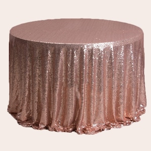 May include: A rose gold round tablecloth made of sequins. The tablecloth has a gathered edge and is perfect for a wedding or special event.