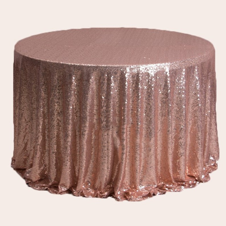 May include: A rose gold round tablecloth made of sequins. The tablecloth has a gathered edge and is perfect for a wedding or special event.