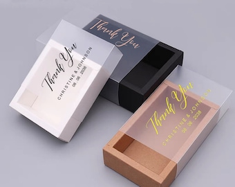 May include: Three rectangular sliding gift boxes with translucent sleeves. One white box has black text, one black box has rose gold text, and one brown box has gold text. Each sleeve features the words Thank You, Christine & Johnson, 08.06.2038.