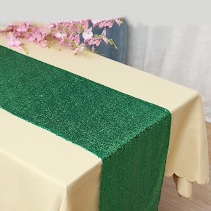 Puede incluir: Un mantel crema con un camino de mesa verde brillante en el centro. Flores rosas adornan la mesa. El verde brillante del camino de mesa contrasta con la tela crema.