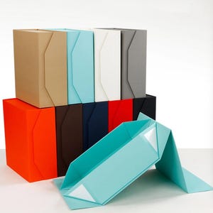 May include: A collection of rectangular foldable gift boxes in various solid colors including tan, light blue, white, gray, orange, brown, dark blue, red, and black, with one light blue box displayed in an open, unfolded position.