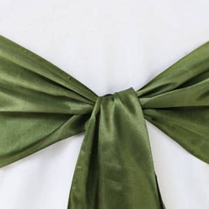 Puede incluir: Una faja de silla de satén verde atada en un lazo. La faja es una forma sencilla y elegante de añadir un toque de color a la decoración de tu boda o evento.