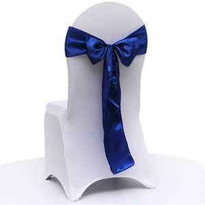 May include: A white chair cover with a vibrant blue satin bow tied at the back. The bow's long tails cascade down the chair, creating an elegant and decorative look. Ideal for weddings and special events.