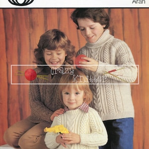May include: Three children wearing knitted sweaters. The child in the middle is holding a toy gun. The child on the right is holding a red ball. The sweater pattern is a cable knit. The text on the image reads "Sirdar 4289 24-32 Aran".