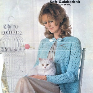 Peut inclure: Une femme portant un cardigan en crochet bleu clair avec un chat blanc assis sur ses genoux. Le cardigan a un motif ajouré et est ouvert sur le devant. La femme est assise sur une chaise avec une cage à oiseaux blanche en arrière-plan. L'image provient d'un livre de modèles de tricot vintage.