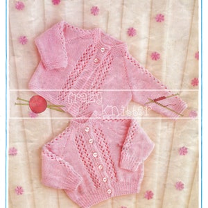 May include: A pink knitted baby cardigan with a button closure and a lacy pattern. The cardigan is laid out on a white background with pink flowers.
