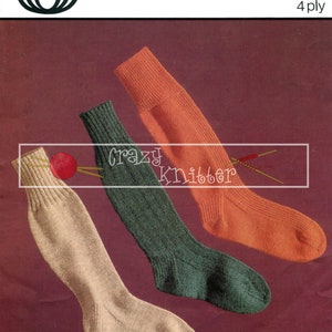 Pode incluir: Três pares de meias de tricô em bege, verde e laranja. As meias estão dobradas e dispostas sobre um fundo bordô. A imagem inclui o texto "5314 10-10 1/2-11 4 ply" e um logotipo para "Sirdar".