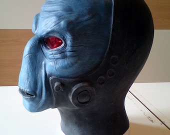 May include: A blue and black latex mask with a detailed face and red eyes. The mask is designed to look like an alien creature.