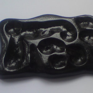 May include: A glossy, black, rectangular object with an organic, flowing design. The surface features a series of rounded, recessed shapes. The overall form is smooth and polished, suggesting a decorative or functional item.