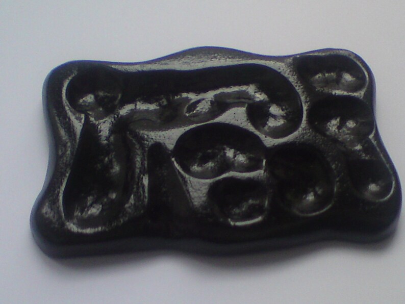 May include: A glossy, black, rectangular object with an organic, flowing design. The surface features a series of rounded, recessed shapes. The overall form is smooth and polished, suggesting a decorative or functional item.