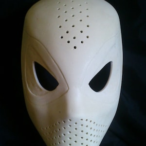 Puede incluir: Una máscara de plástico blanca con una superficie texturizada y múltiples agujeros pequeños. La máscara tiene dos agujeros para los ojos y un agujero para la boca.