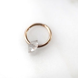 Op de afbeelding: Een gouden oorring met een heldere, diamantvormige kristallen hanger.