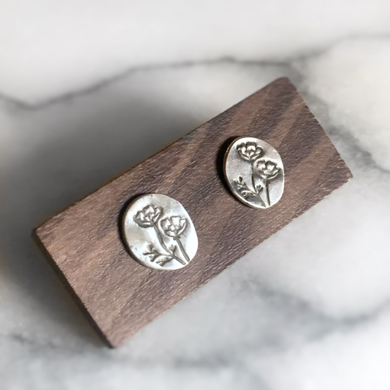 May include: A pair of silver earrings with a floral design. The earrings are oval shaped and have a hammered texture.