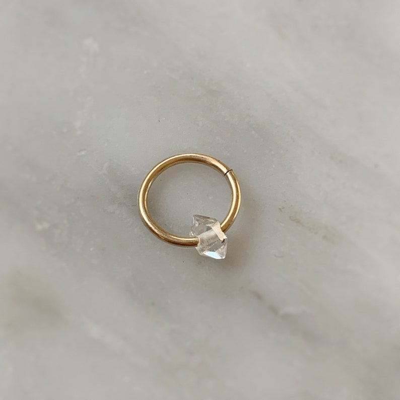 Op de afbeelding: Een gouden oorring met een heldere kristallen edelsteen.